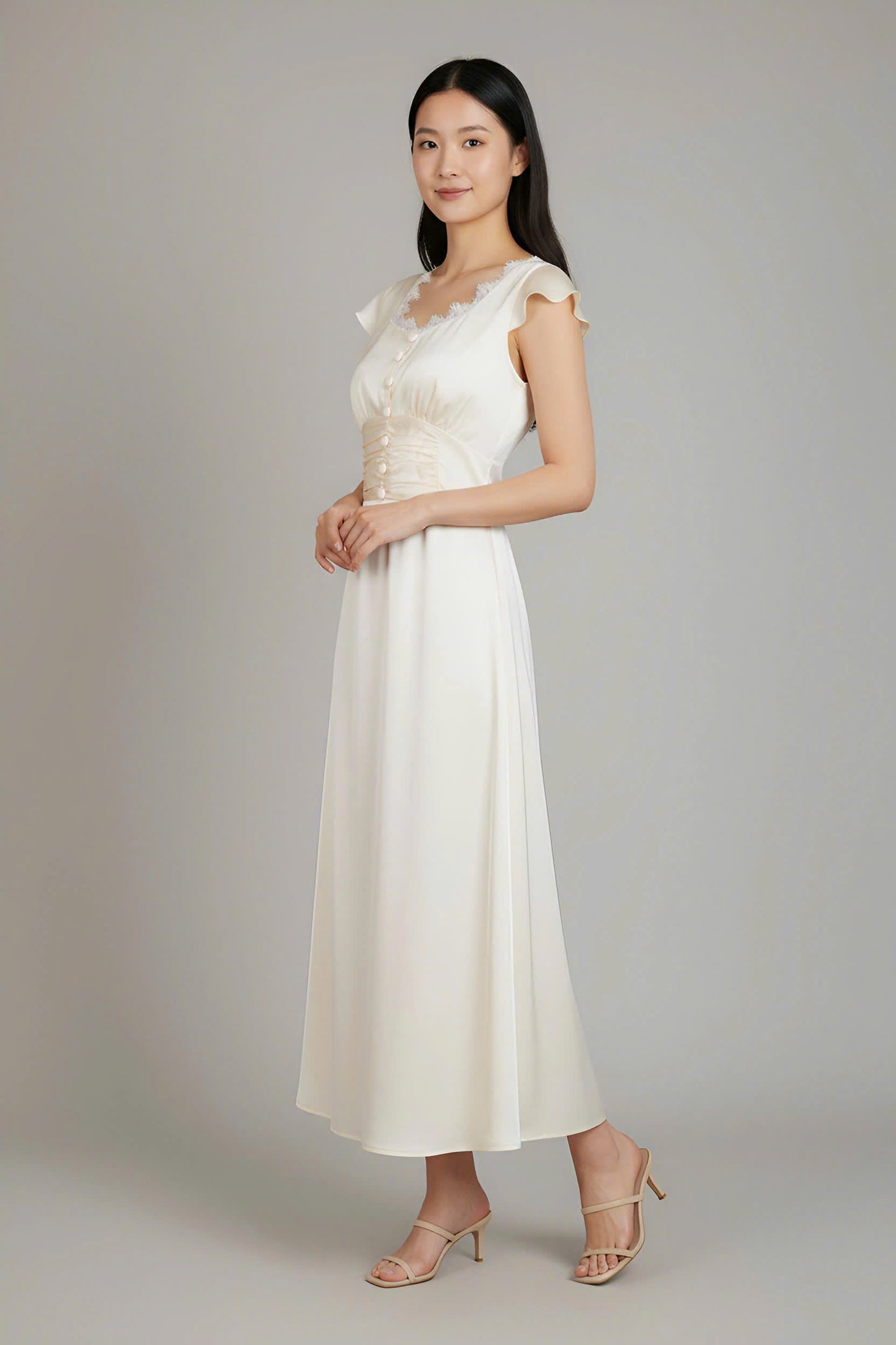 Woman wearing a white dress with lace details on a plain background